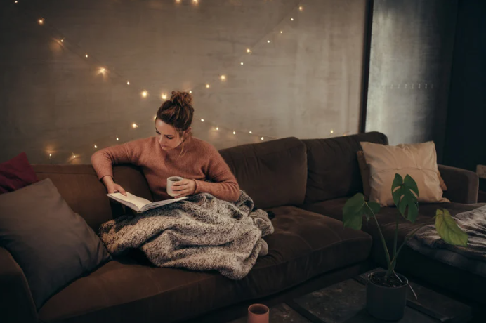 woman sitting on couch with a book and tea, very cozy